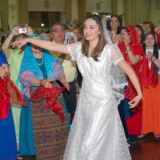 An actress bride dances as in-laws and friends, wearing traditional Armenian clothing, clap and cheer.