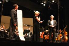 Lynne Ludeke, center, expresses thanks to conductor Theodore Stern, right, while Chris Krambo displays a list of more than 300 works the orchestra has presented over the years.