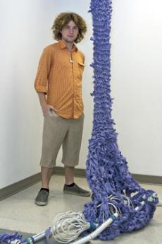 NOTHING BUT NET:  Paul Petros stands next to his creation, Entrapment of the Utilitarian Man at the GCC Annual Student Art Exhibition. See related story and photos, pages 10-11.