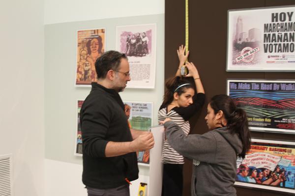 ART EXHIBIT: Students Anai Cosenza and Lavinia Aghakhani assist director David John Attyah to install the latest exhibit at the Art Gallery